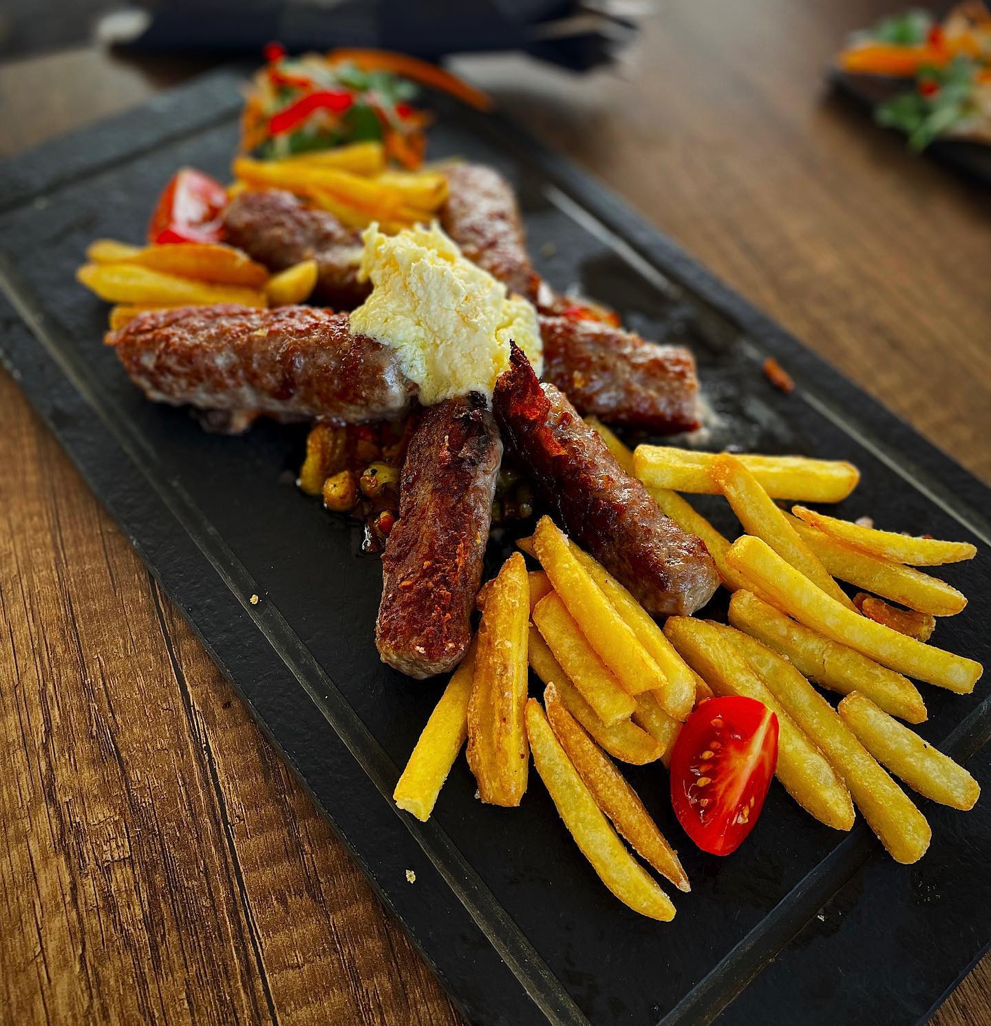 A plate of grilled ćevapčići served with french fries and a dollop of kajmak.