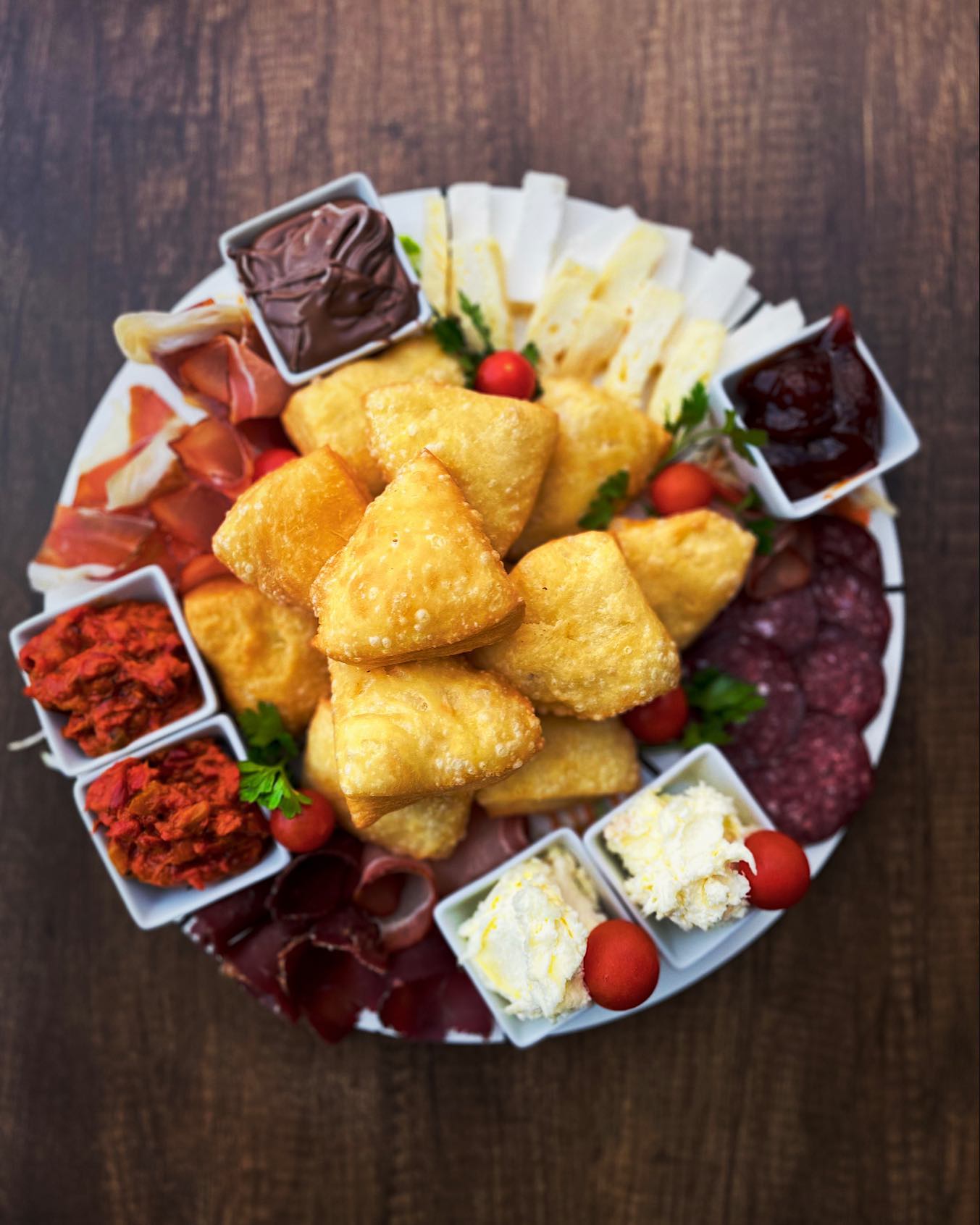 An overhead view of a traditional Serbian meze platter with fried dough, cured meats, and cheeses.