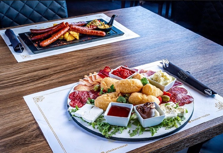 A platter of Serbian meze including uštipci, prosciutto, cheese, and various dips.